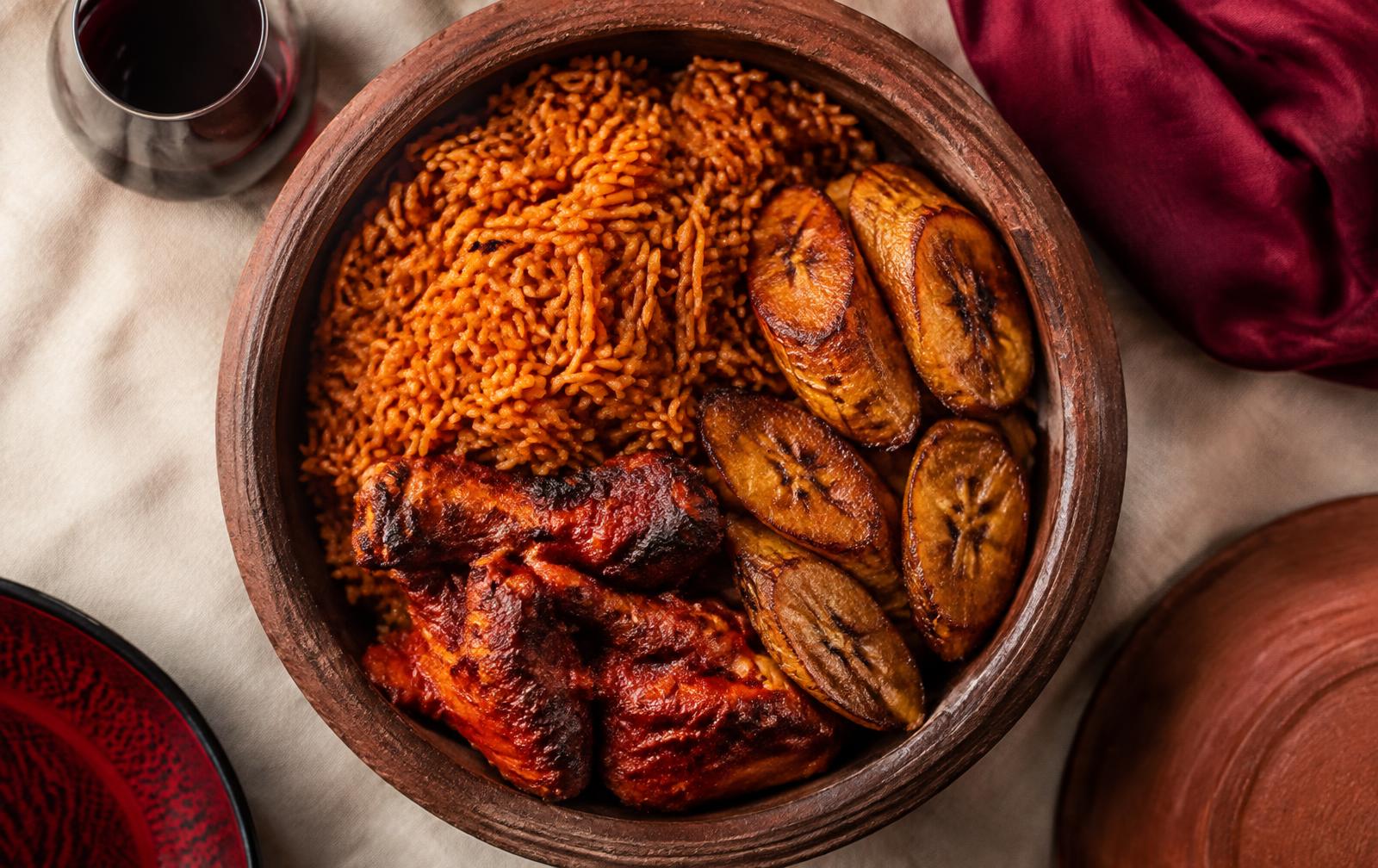 Smokey jollof rice with peppered chicken and fried plantain in a clay pot